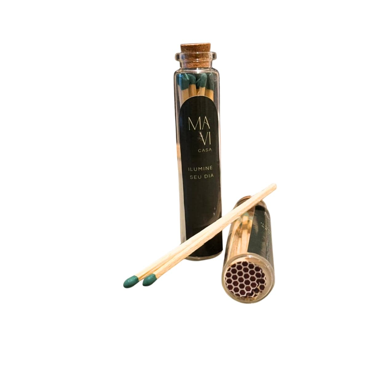 Kit Acenda Mavi Casa: potinho de vidro com tampa de rolha e rótulo preto “ilumine seu dia”, um segundo potinho deitado mostrando o riscador colmeia na base e dois fósforos de cabeça verde à frente